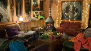 A photo of the fire area in the circular bar at Coed Hills. Taken at night with fairy lights and comfortable sofas arranged around a large woodburning stove. There is a large, striking painting on the wall and it is a very evocative image of a magical place.