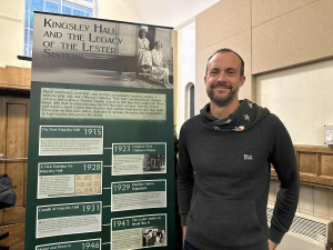 Rob Sage photo of Rob Sage by a banner with history of Lester sisters who founded Kingsley Hall