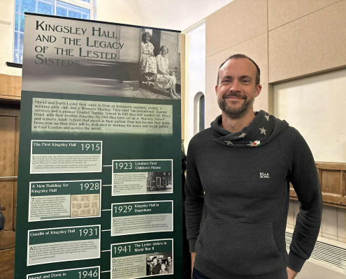 photo of Rob Sage by a banner with history of Lester sisters who founded Kingsley Hall