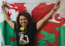 Amuta Garud with her arms in the air and a Welsh flag behind her