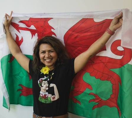 Amuta Garud with her arms in the air and a Welsh flag behind her