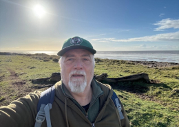 Andy Chyba looking at the camera with a blue sky and seascape behind him