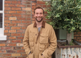photo of chance standing in front of a brick wall wearing a brown coat and a broad smile