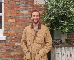 Chance photo of chance standing in front of a brick wall wearing a brown coat and a broad smile
