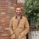 photo of chance standing in front of a brick wall wearing a brown coat and a broad smile